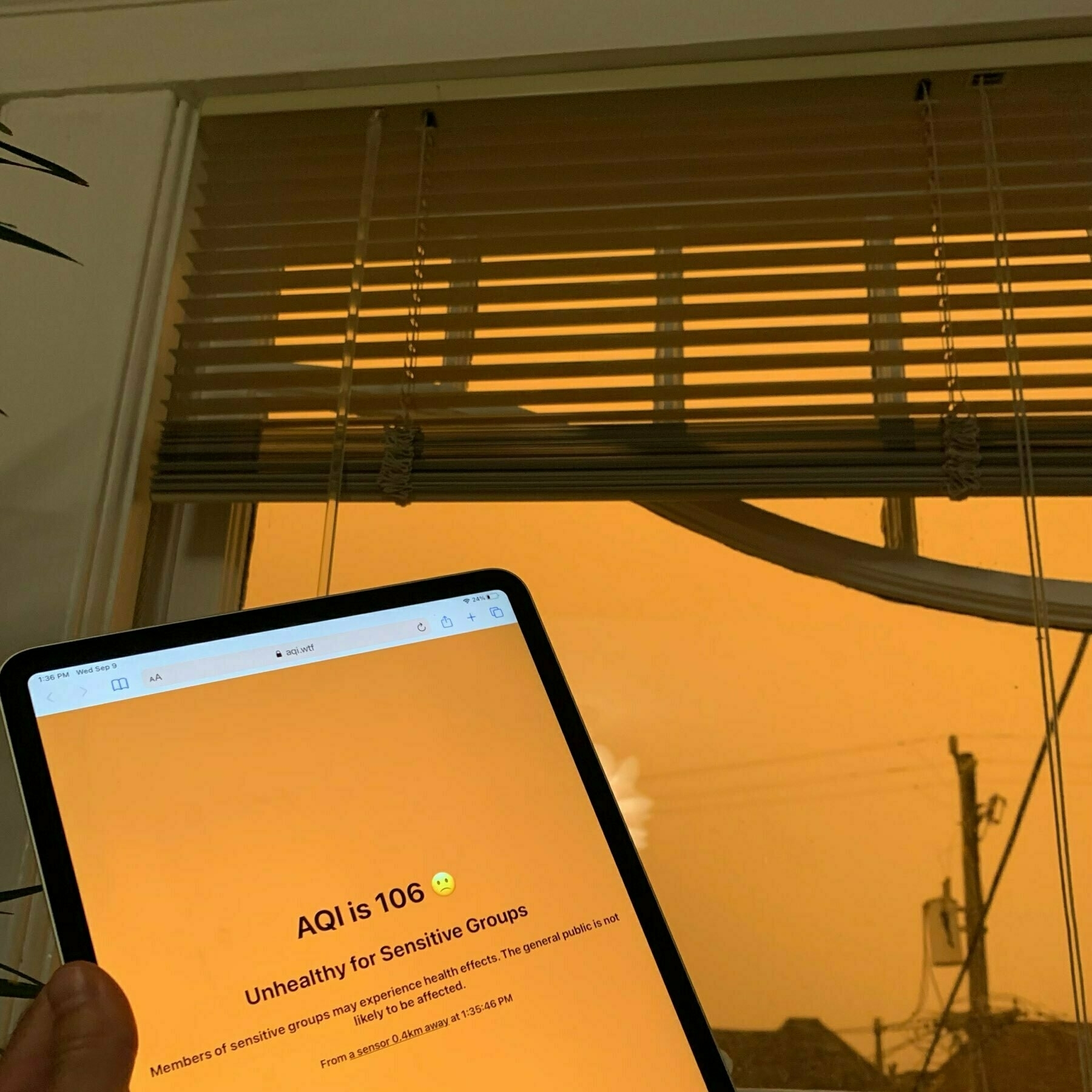 iPad open to aqi.wtf showing an orange AQI in front of a window with orange sky