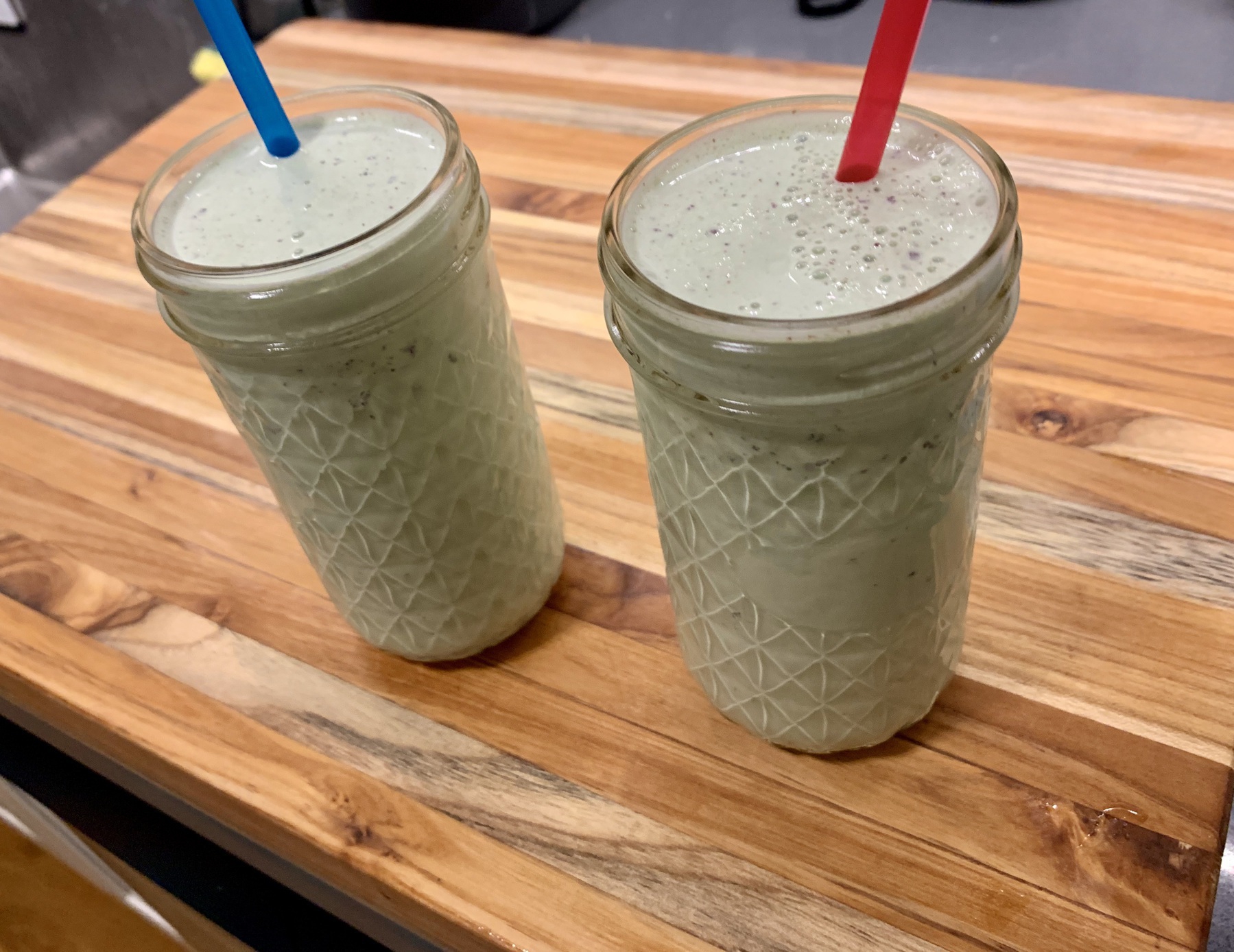 Two mint green milkshakes in glasses with straws on a wooden board