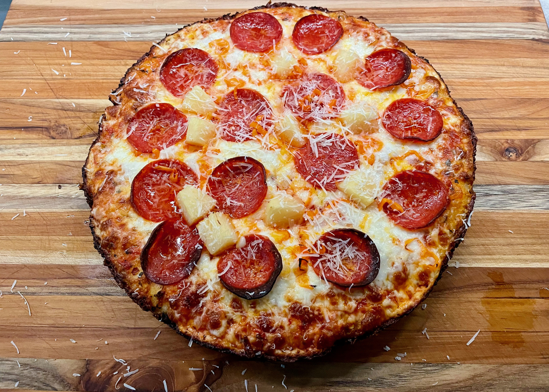 A pan pizza with pepperoni, pineapple, and habaneros on a cutting board